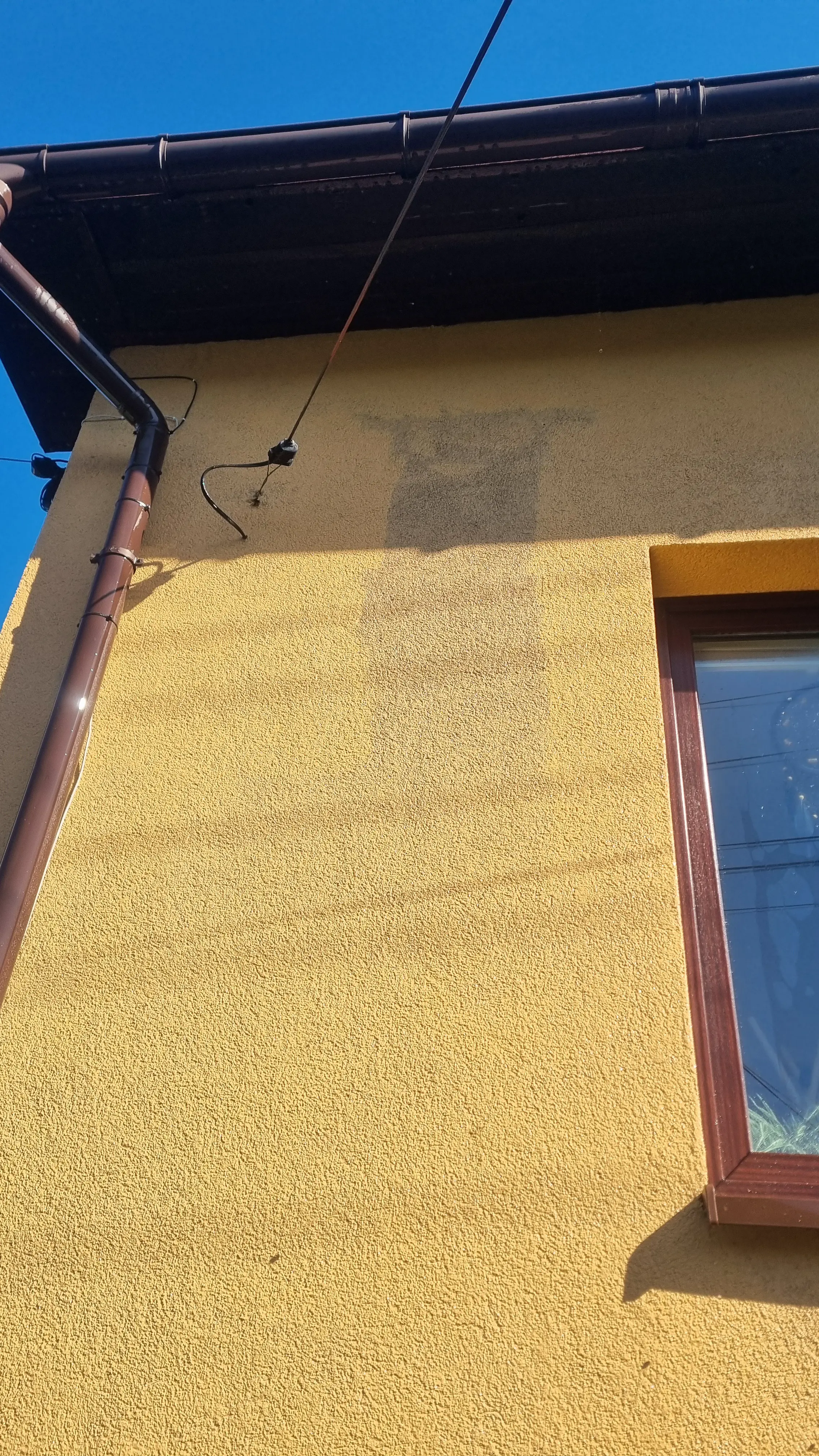 Zabrudzona elewacja budynku przed myciem, widoczna plama na żółtej farbie
