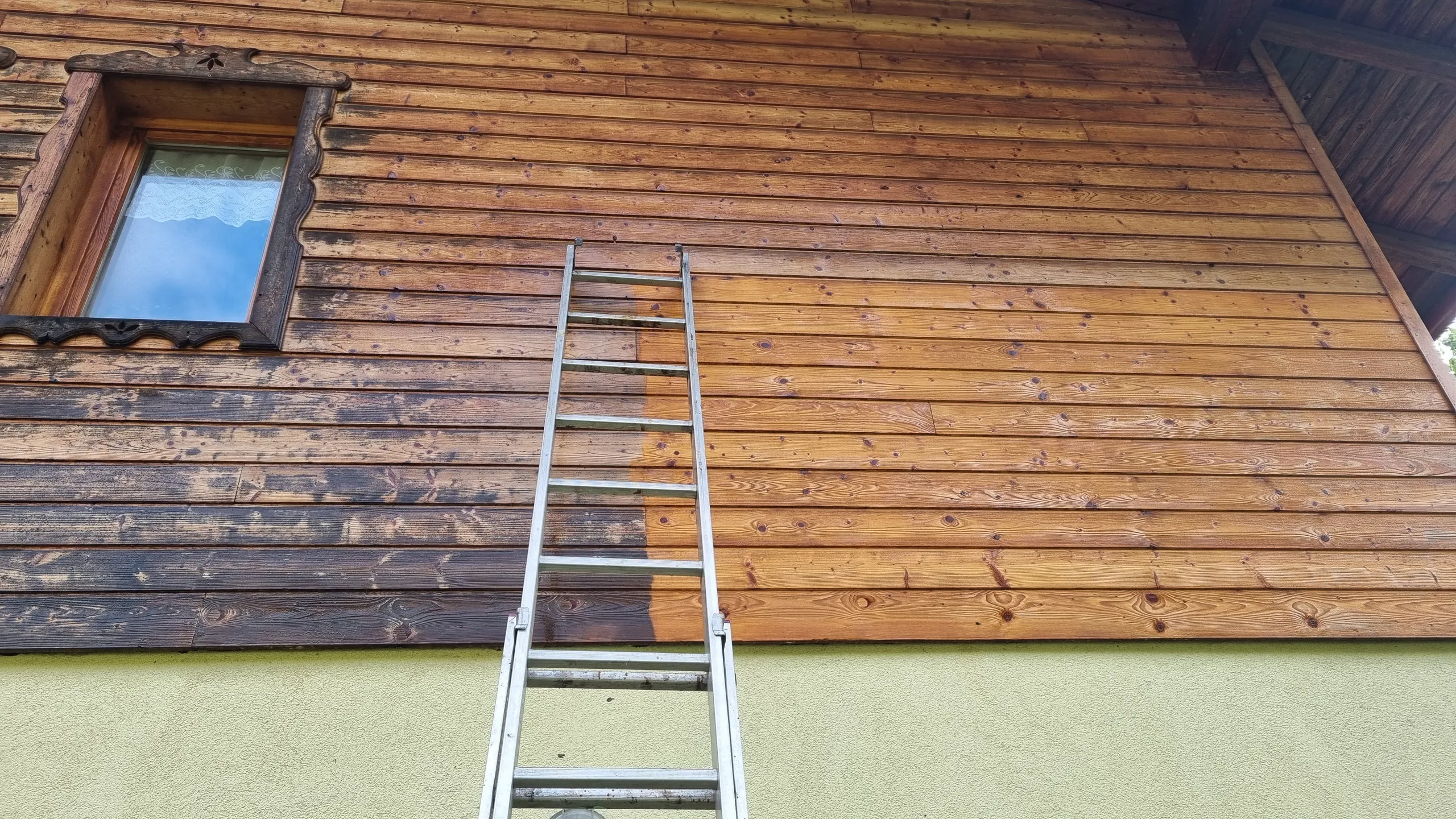 Malowanie elewacji drewnianej budynku przy użyciu drabiny